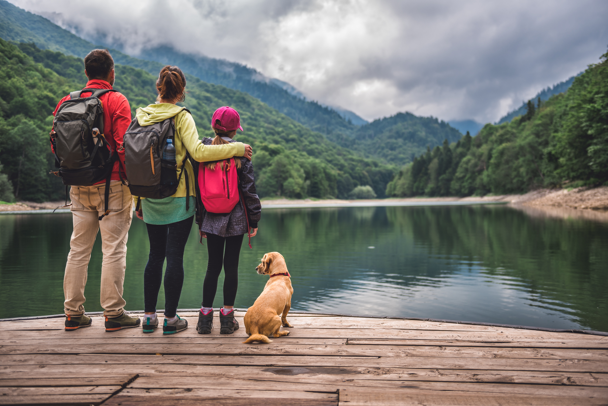 a family in hiking gear stands on a dock looking out over the water