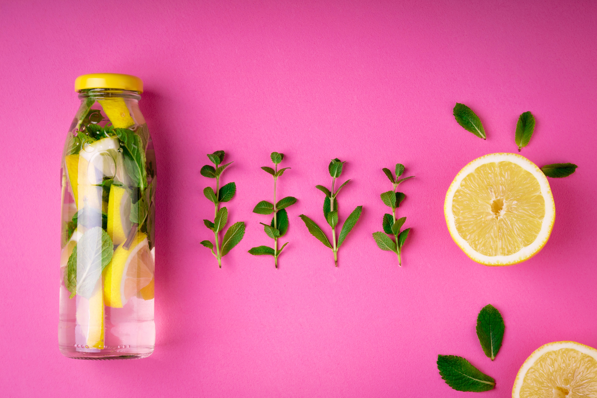 A bottle of lemon infused water on a pink background 