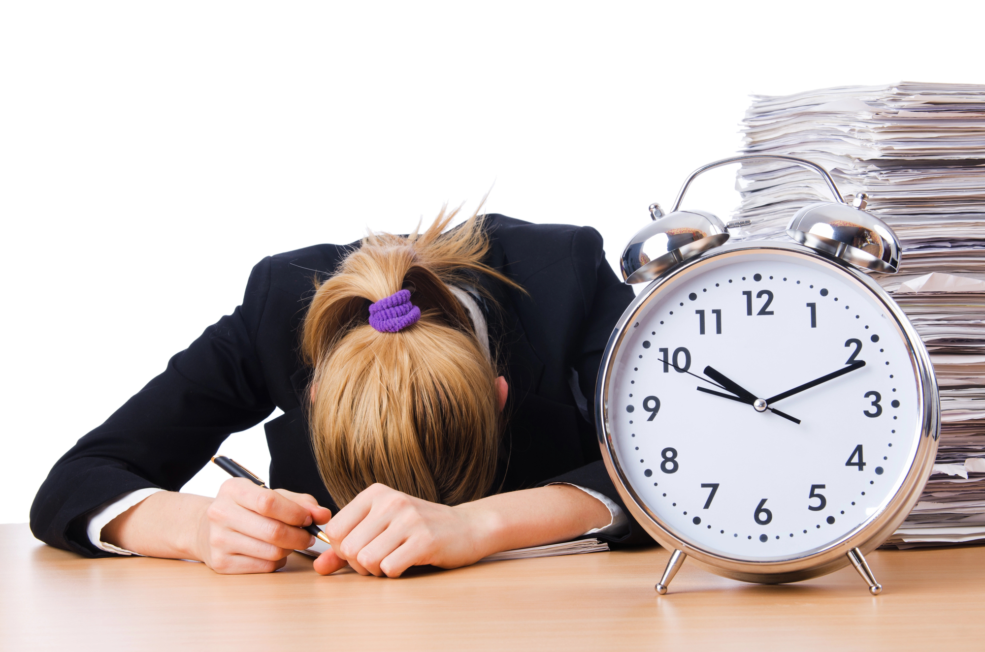 A woman in a business suit asleep at her desk behind an alarm clock