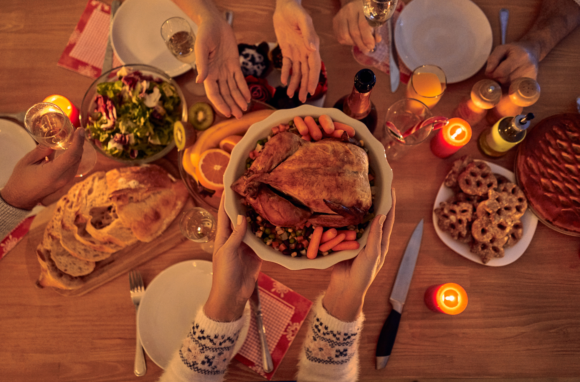 hands hold out a turkey over a festive holiday dinner table