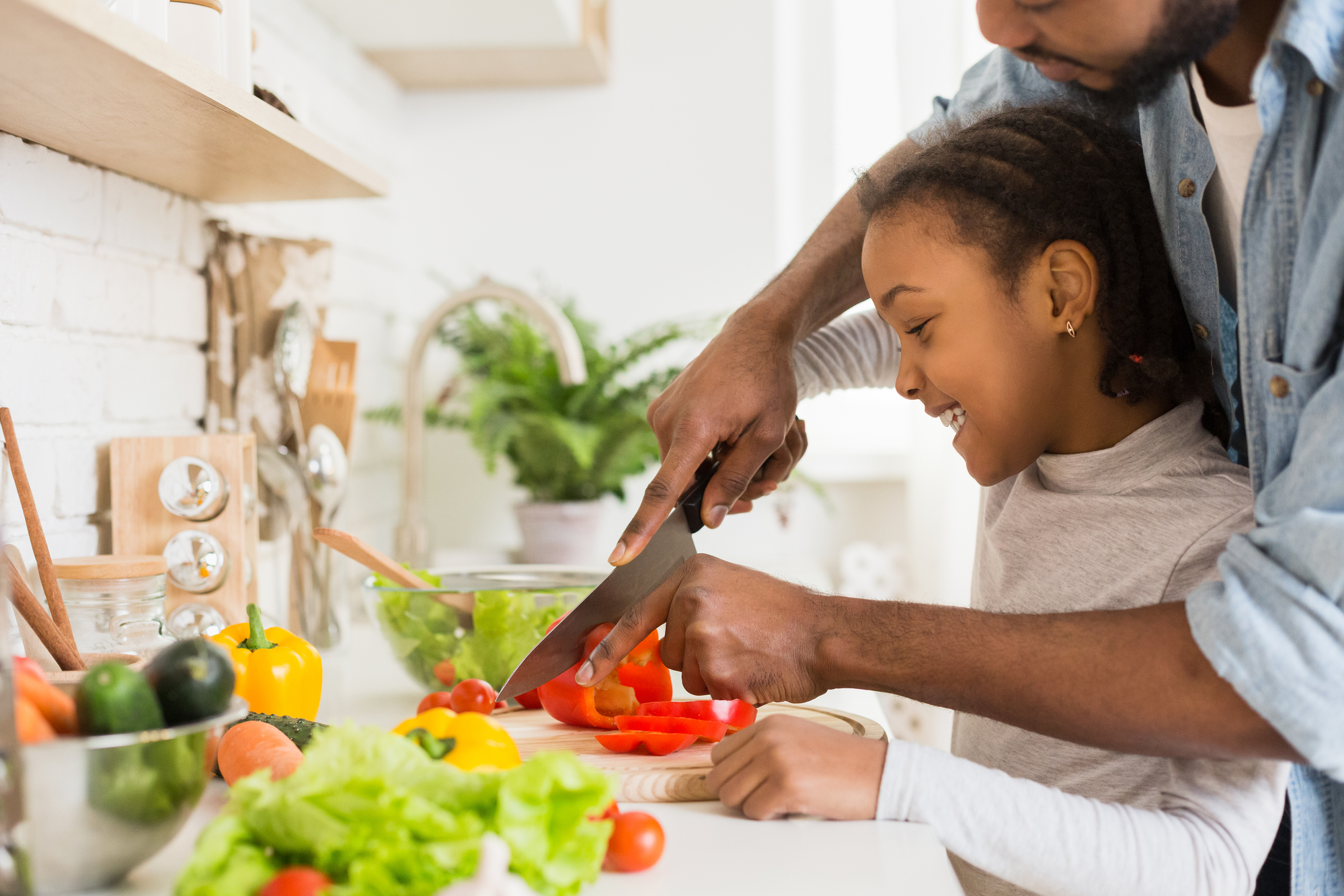 a father and daughter chop veggies on a counter together