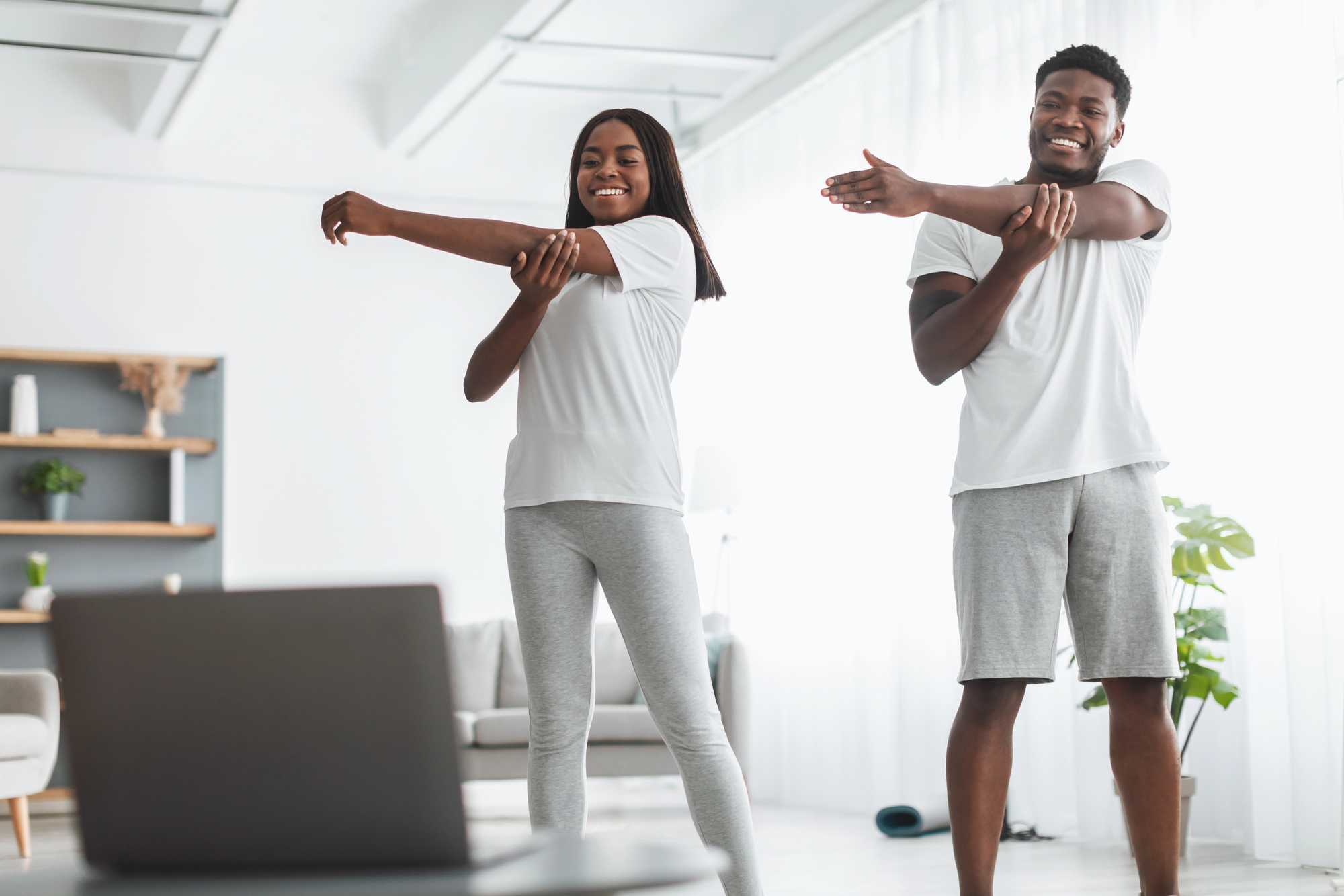 A man and woman follow a workout video on a laptop together