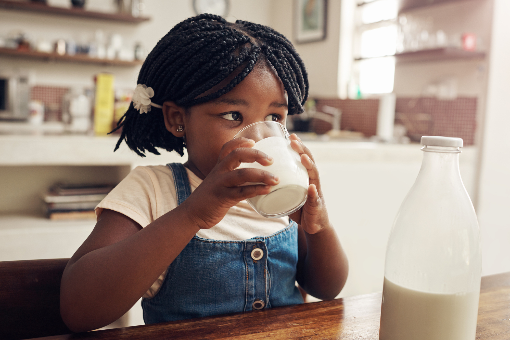 A little girl drinking a glass of milk at a table