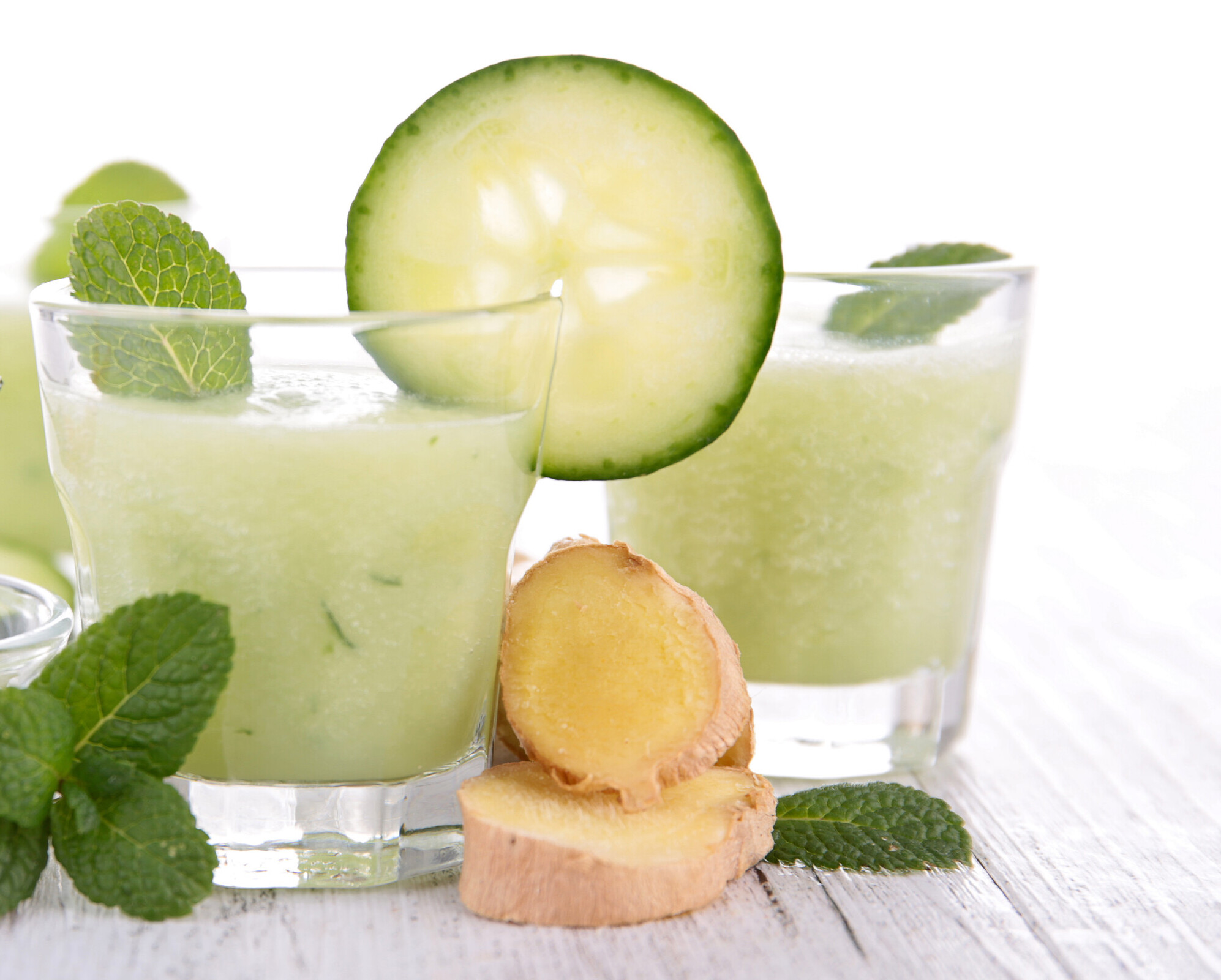 Clear glasses filled with light green beverage, flanked by ginger root and accented with mint leaves.