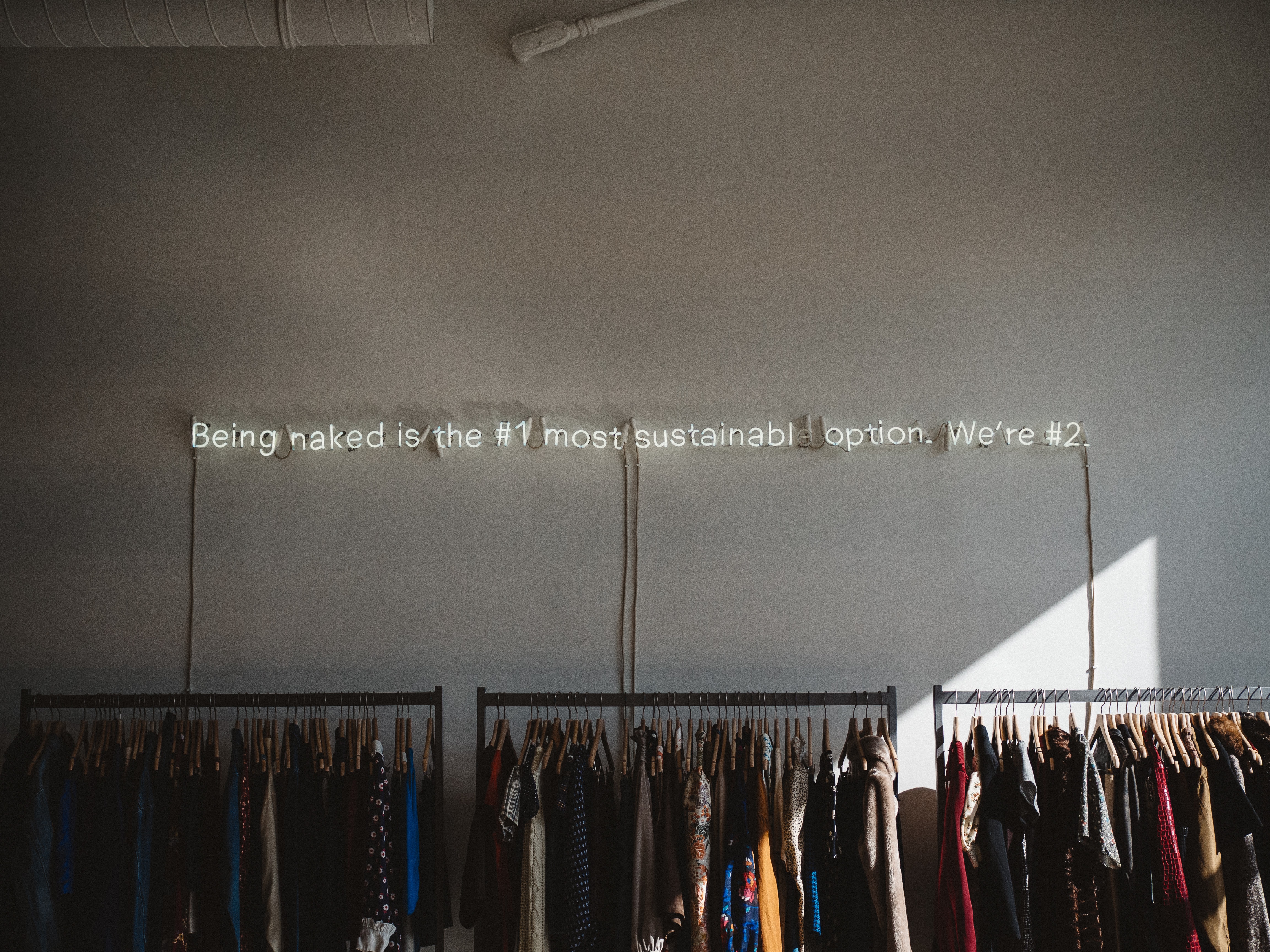 Sustainability in the Fashion Industry: Clothes rack with sign above reading "Being naked is the #1 most sustainable option. We're #2."