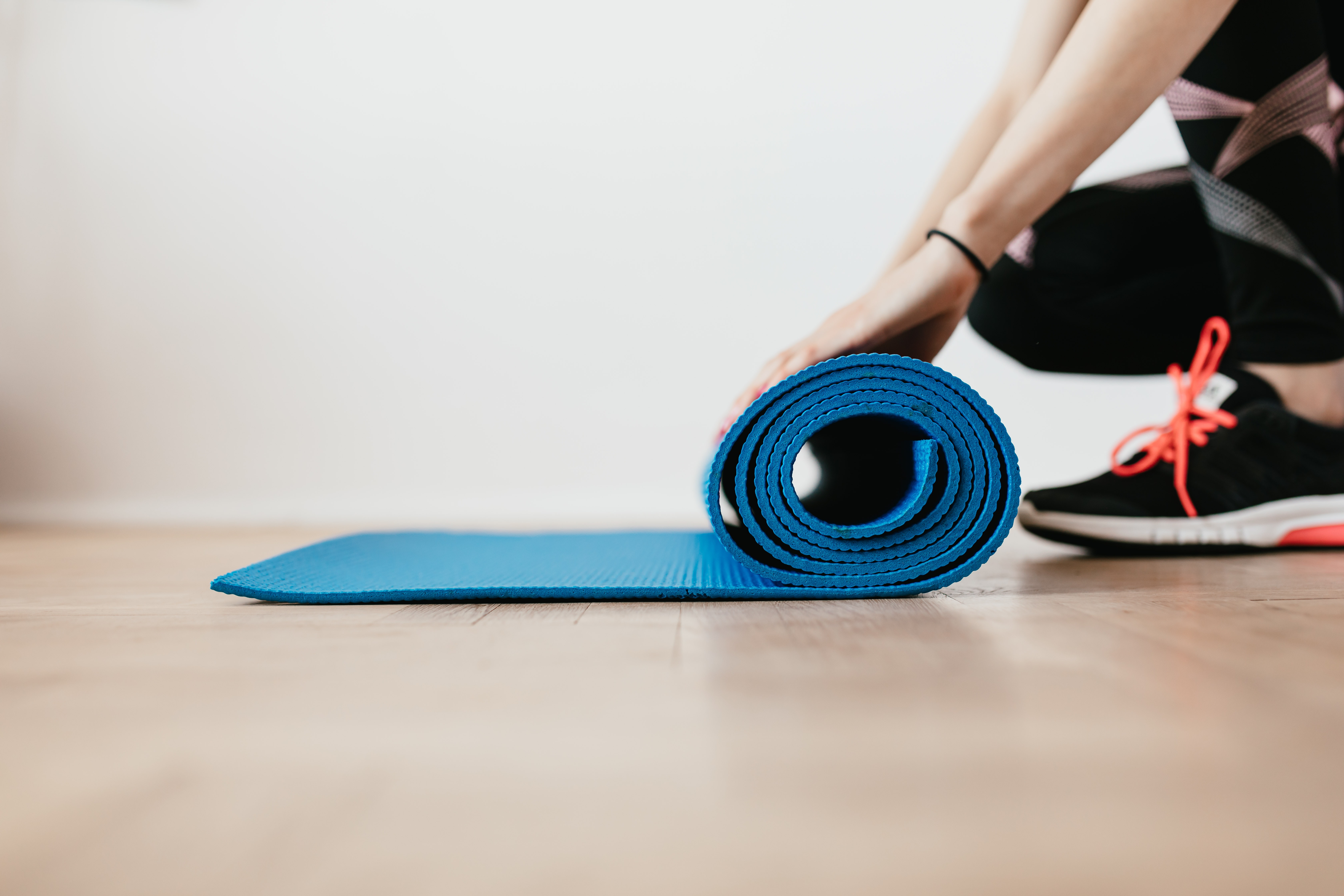 a woman wearing running shoes unrolls a yoga mat
