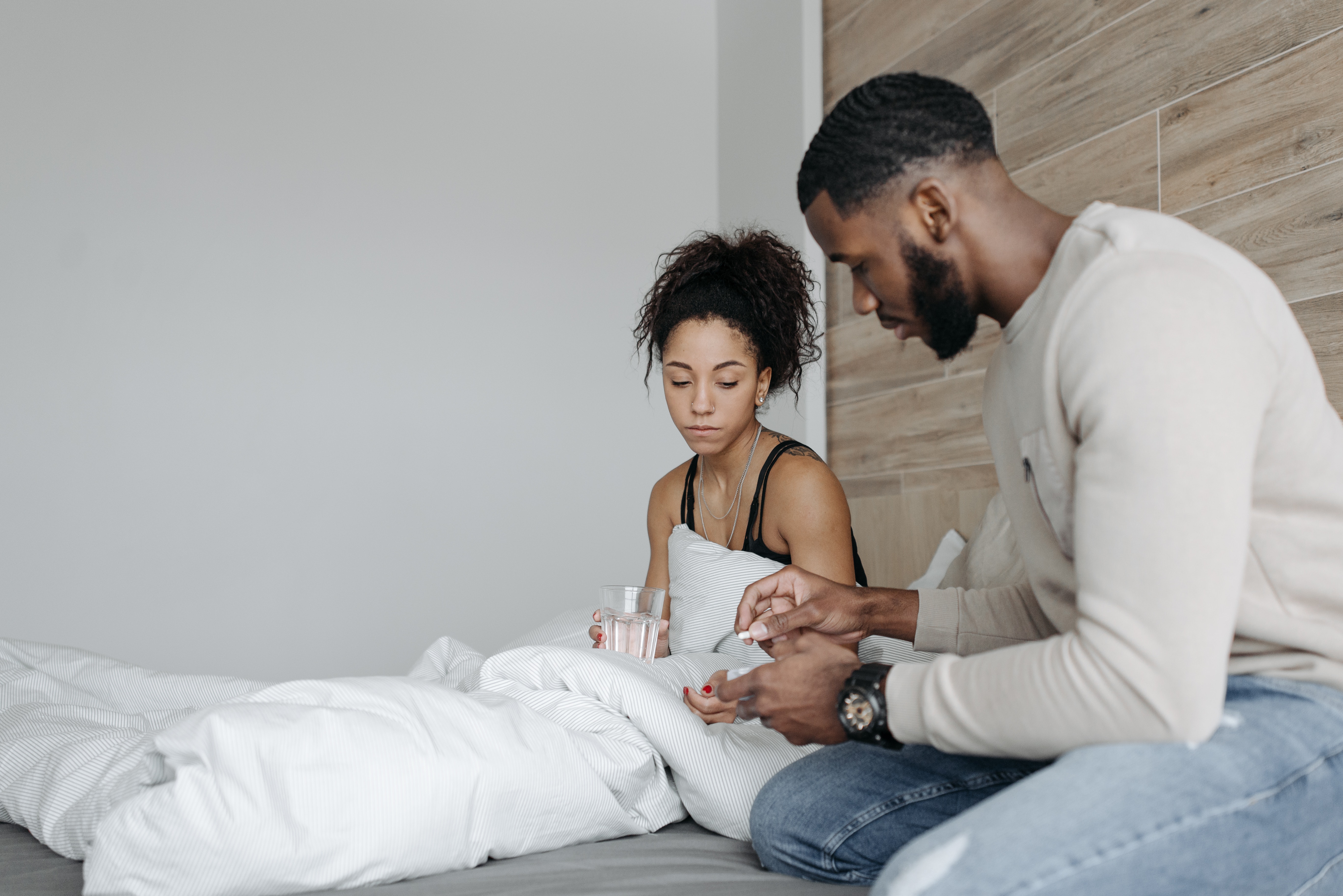 man giving woman in bed a white pill to take