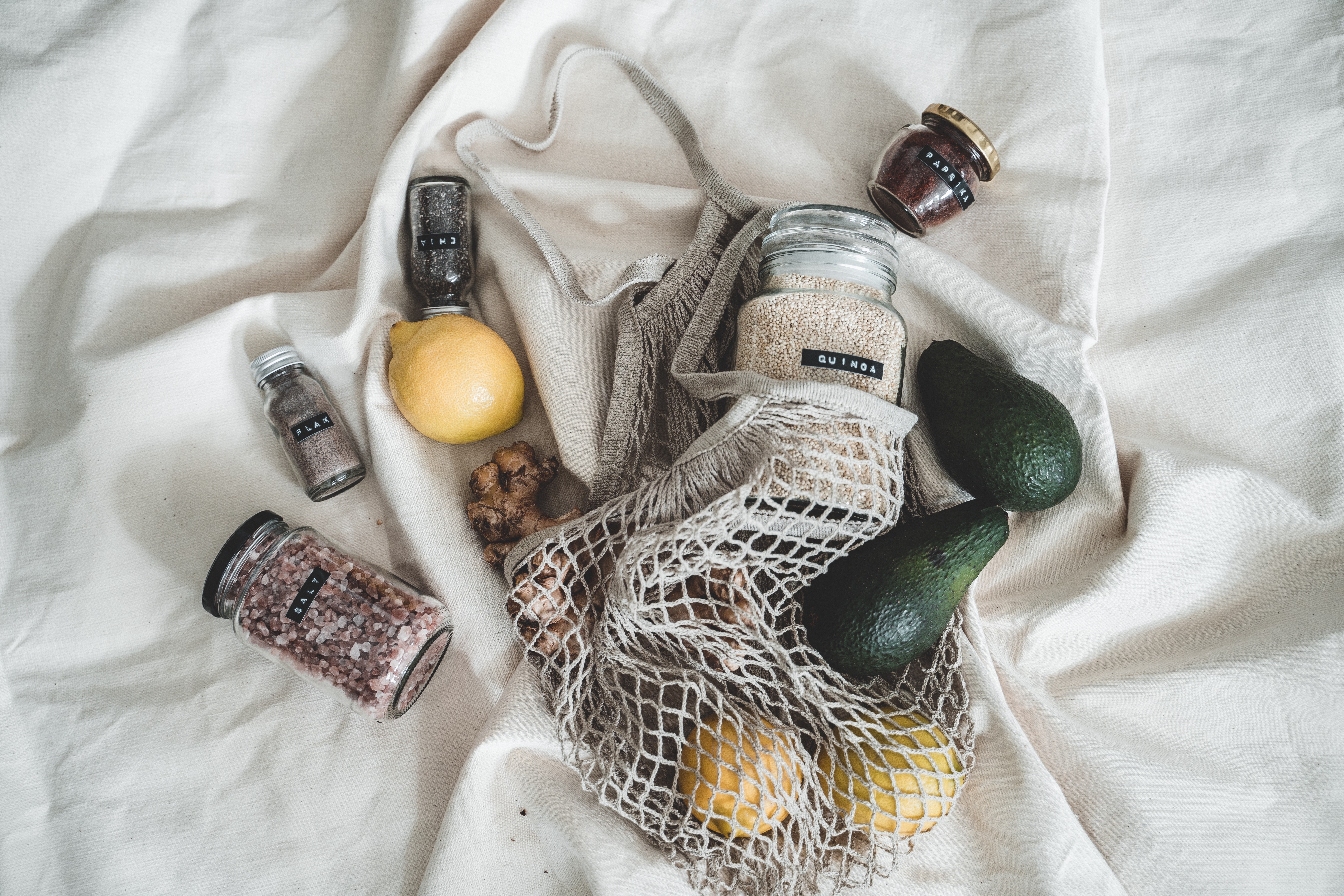 reusable bag with lemons, avocados, and jarred spices laying on a bed
