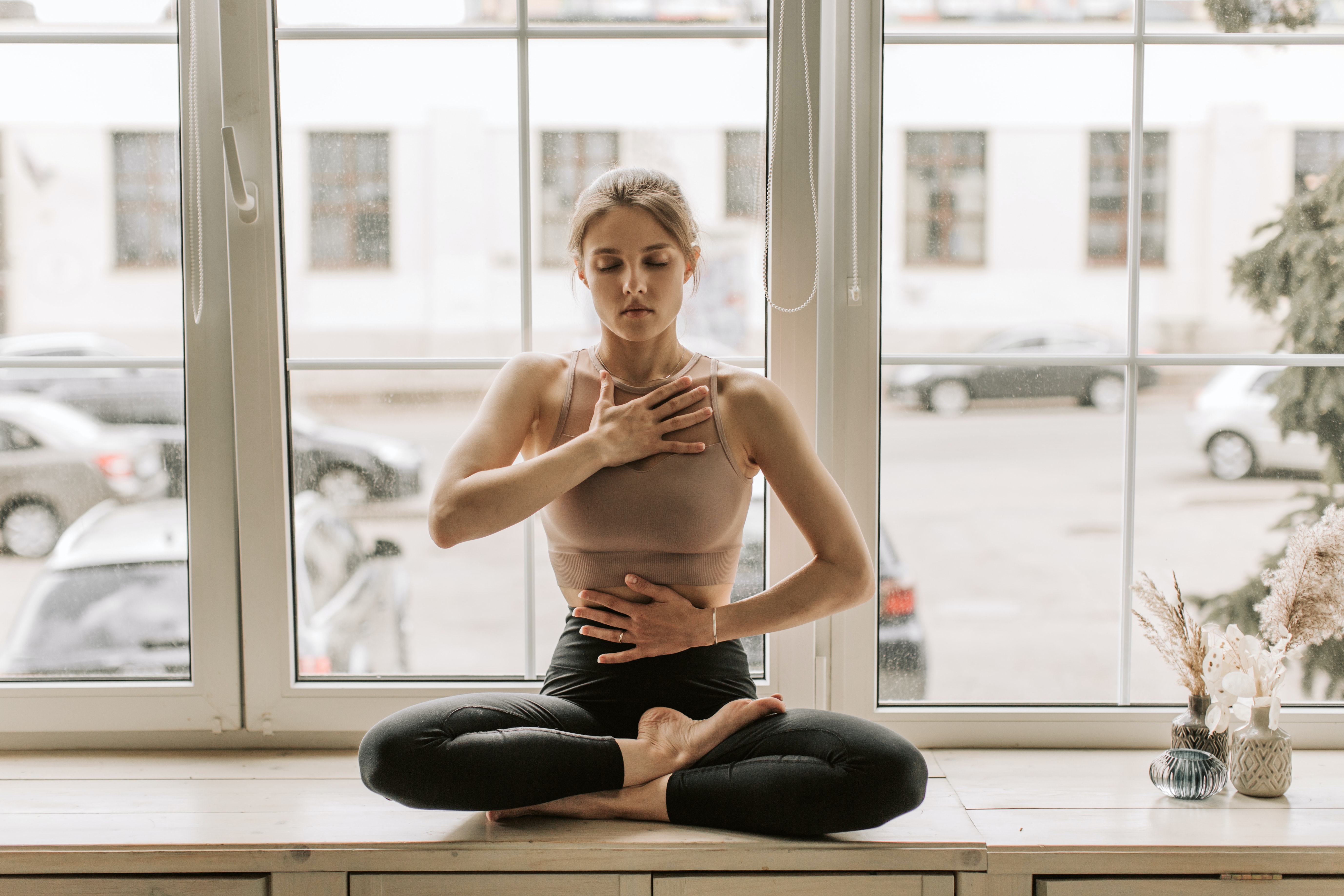 woman crossed legged with one hand on chest and one hand on stomach practicing breathwork