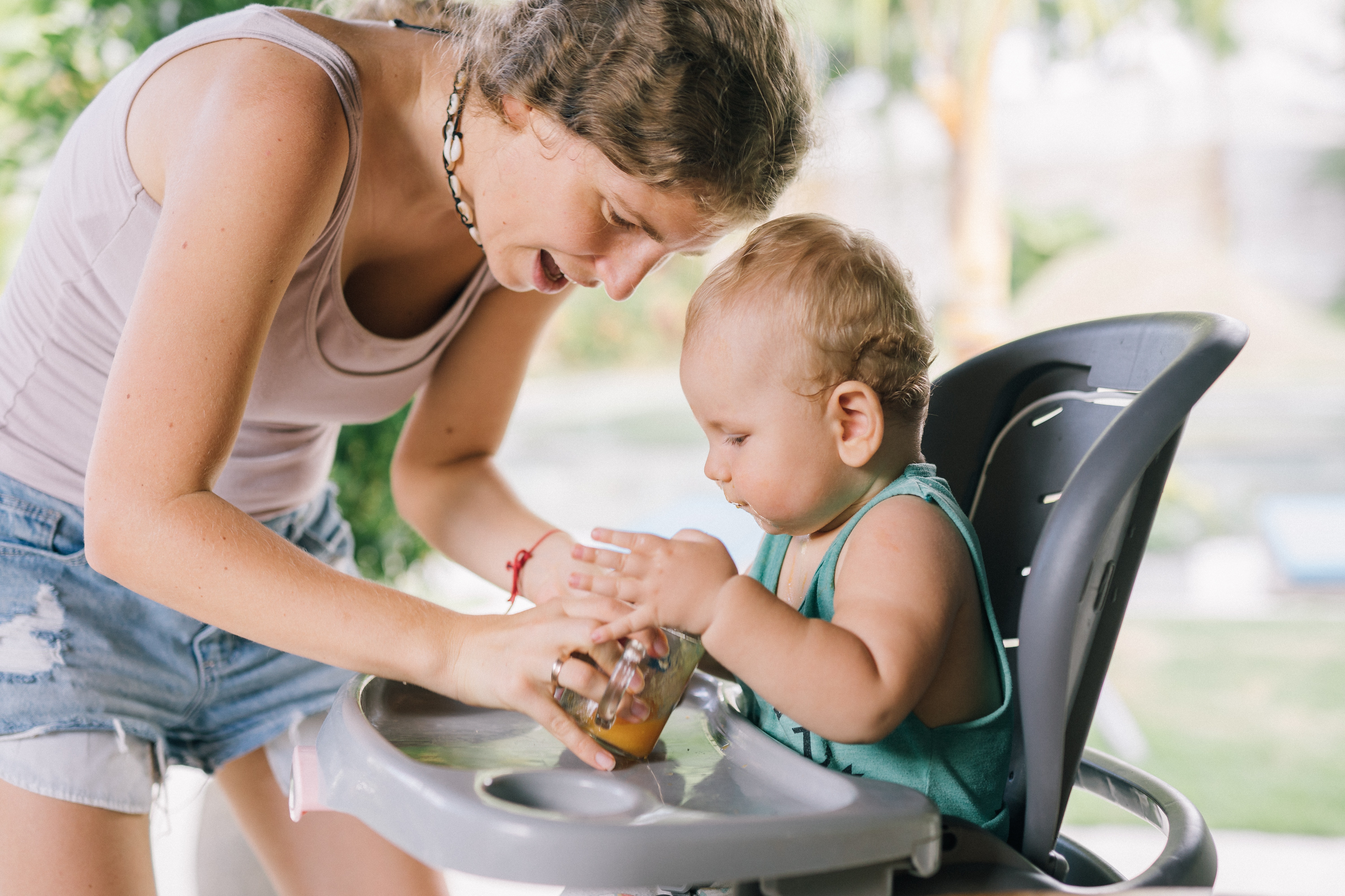 mother helping baby with food in a high chair