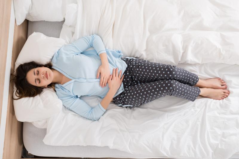 Natural Remedies to Help with Period Cramps: woman lying on bed holding her stomach