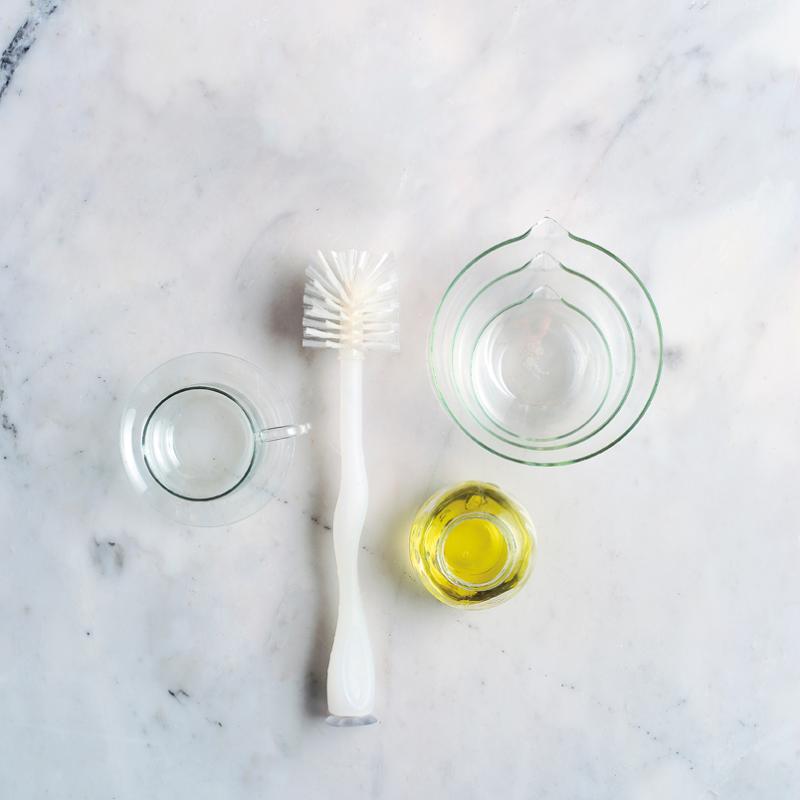 clear bowls, a scrubber, and cleaning solution on a white marble counter
