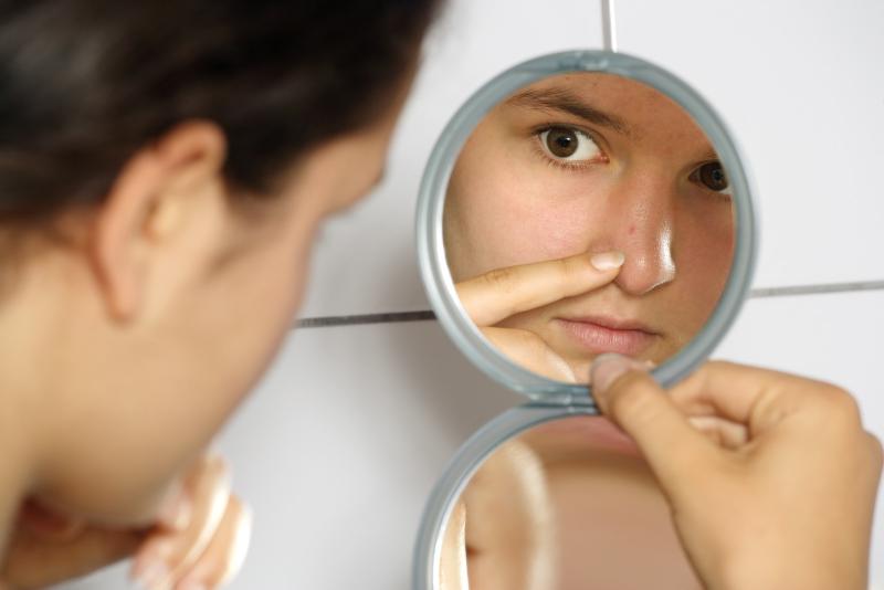 woman closely checking her face in a mirror