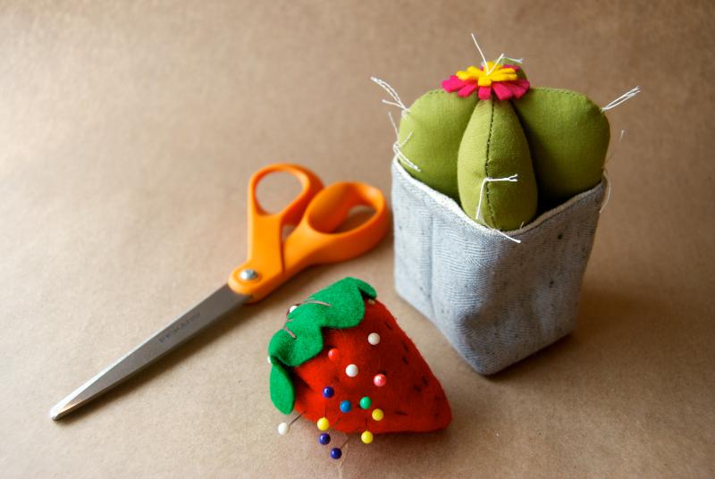 a hand-sewn cactus craft with scissors and a strawberry pin cushion nearby