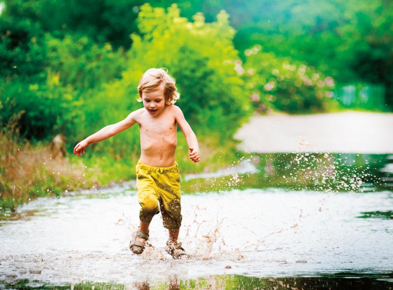 young boy running through a mud puddle