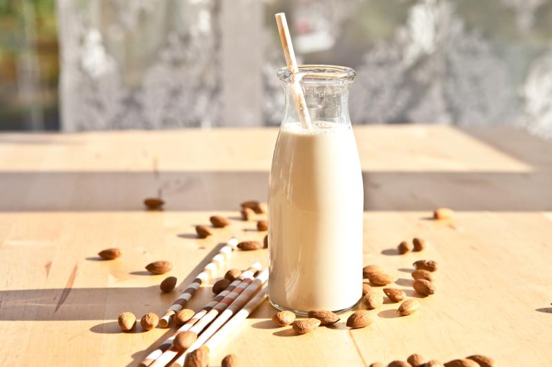 glass bottle of nut milk with almonds scattered around it
