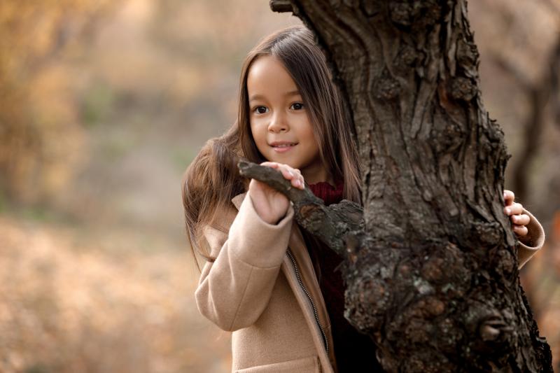 little girl peering around the trunk of a tree