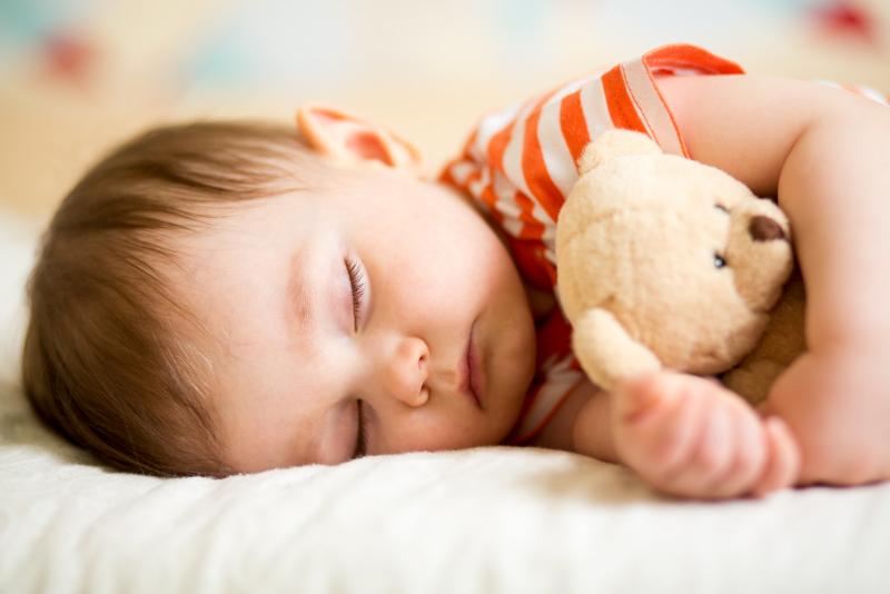A toddler sleeping on his side and hugging a teddy bear