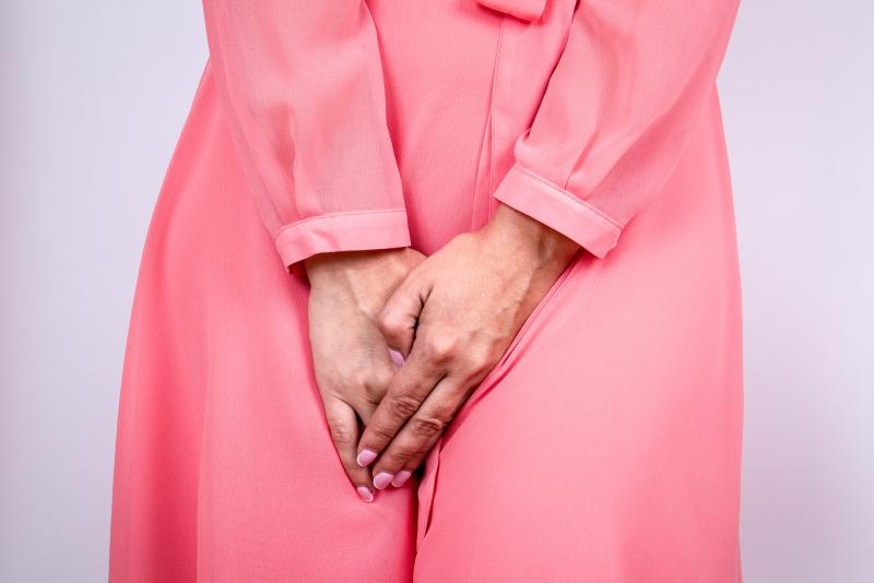 Woman wearing a pink silk dress squeezing her legs together because she has to urinate