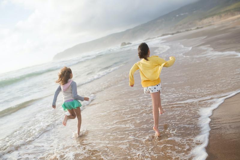 two kids run through the water across a beach's shoreline