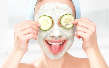 woman with facial mask holding cucumber slices on her eyes and sticking out her tongue