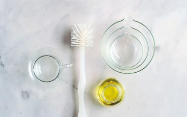 clear bowls, a scrubber, and cleaning solution on a white marble counter