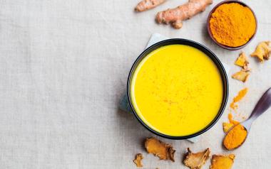 Reduce Inflammation With Food! A Turmeric Coconut Latte Recipe: mug of turmeric latte, fresh turmeric and ground turmeric seen from above on a white tablecloth