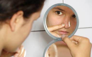 woman closely checking her face in a mirror