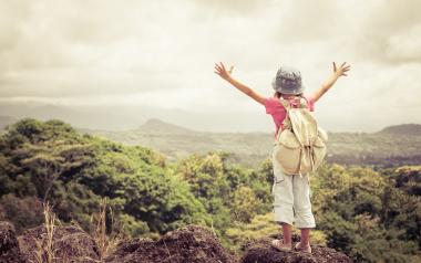 Healthy Challenge or Undue Risk? child with backpack and hat standing atop a high hill