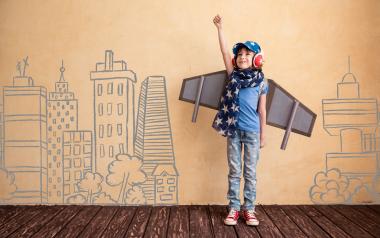 child dressed up with airplane wings against a wall with buildings drawn on it