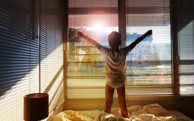young child waking up and stretching while standing on the bed and looking out the window