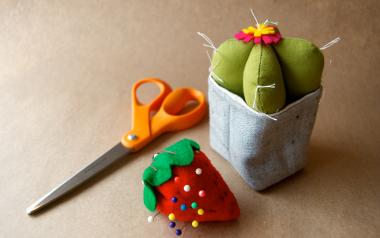 a hand-sewn cactus craft with scissors and a strawberry pin cushion nearby