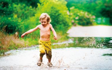 young boy running through a mud puddle