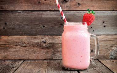 strawberry smoothie in a Mason jar with red striped straw against wooden background