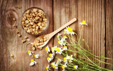 chamomile flowers with dried herbs in a bowl and spoon on a wooden background