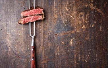 steak pierced by a meat fork on a wooden background