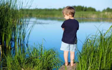 small boy stands beside a pond