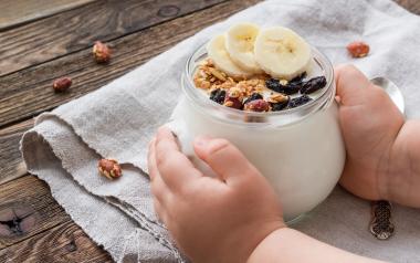 baby's hands holding a bowl of yogurt with fruit and bananas on top