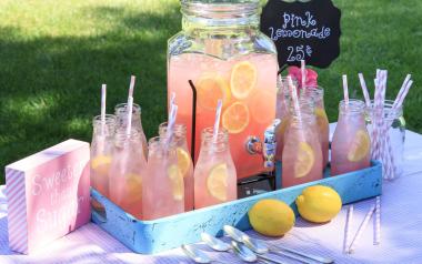 a jar and several glasses of pink lemonade on a picnic table outside