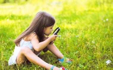 small girl sitting in the grass with a magnifying glass