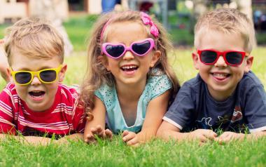 three children wearing sunglasses and lying in the grass on their bellies