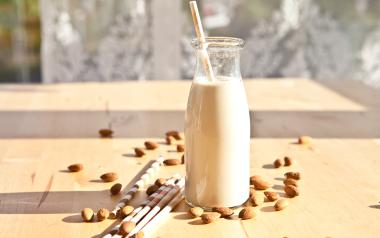 glass bottle of nut milk with almonds scattered around it