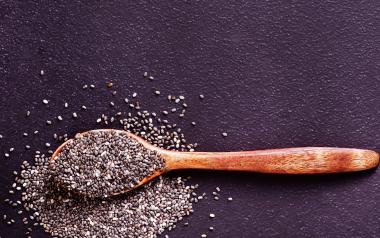 spoonful of chia seeds spilling out onto a black background