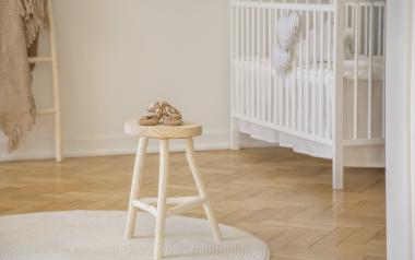baby shoes placed on wooden stool standing in white kid room interior with crib, round rug 