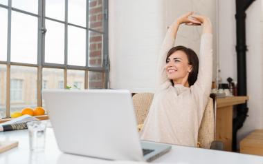 woman stretching arms up in the air in front of her laptop