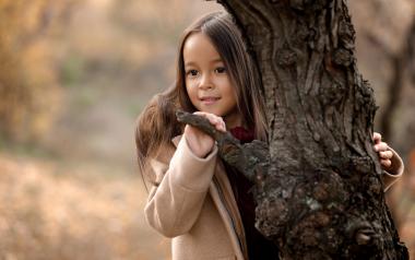 little girl peering around the trunk of a tree