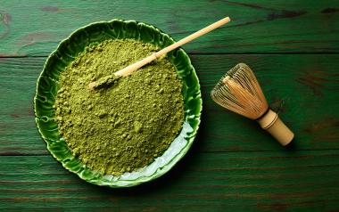 Green powdered matcha in a bowl with a whisk to the side on the table