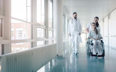 A nurse pushing a woman in a wheelchair down a hospital hallway.