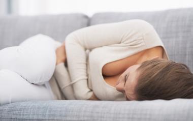 Woman lying on a couch clunching her stomach in pain