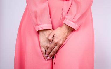 Woman wearing a pink silk dress squeezing her legs together because she has to urinate